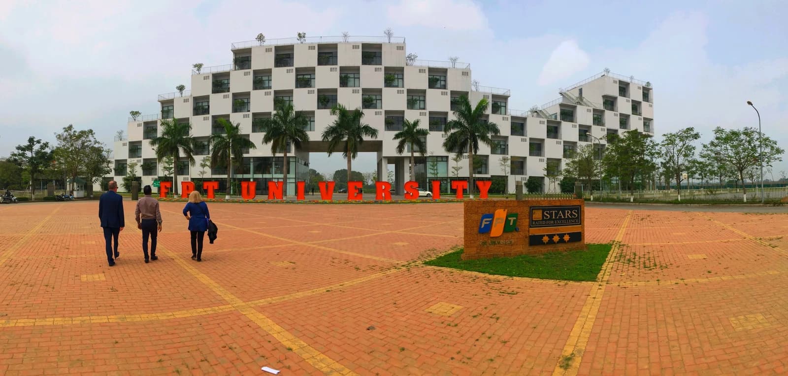 Three individuals walking towards the FPT University administration building entrance.