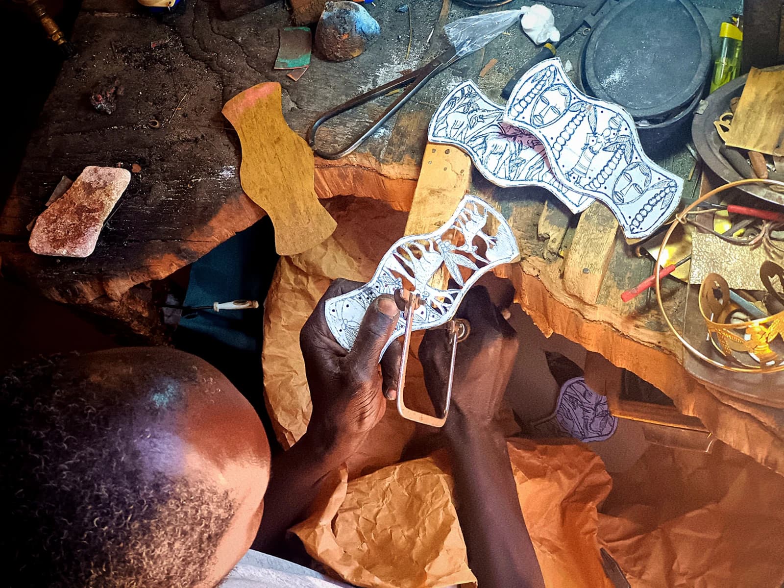 African metalworker's hands crafting decorative metal accessories on a workbench.