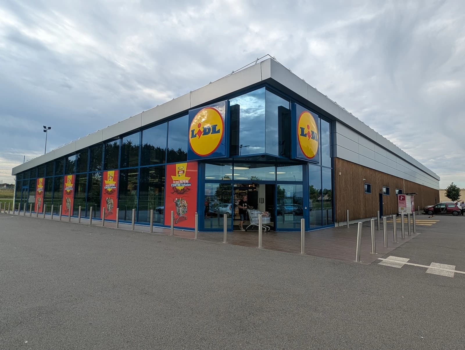 Exterior of a modern Lidl supermarket building with glass and wood facade under a cloudy sky.