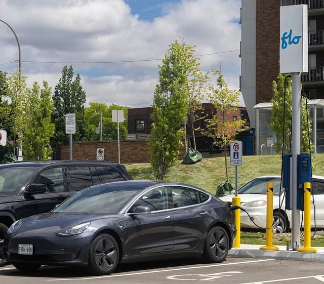 Dark grey Tesla Model 3 sedan charging at a Flo electric vehicle charging station.