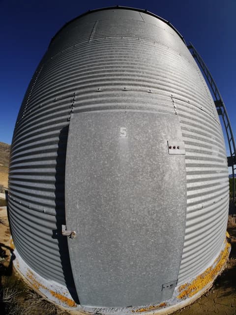 Close-up of a corrugated metal grain silo against a clear blue sky.