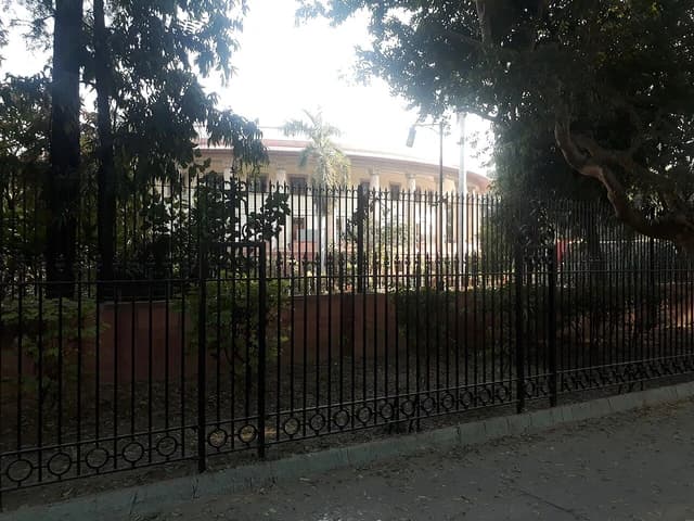 Front view of the Supreme Court of India building seen through trees and a fence.