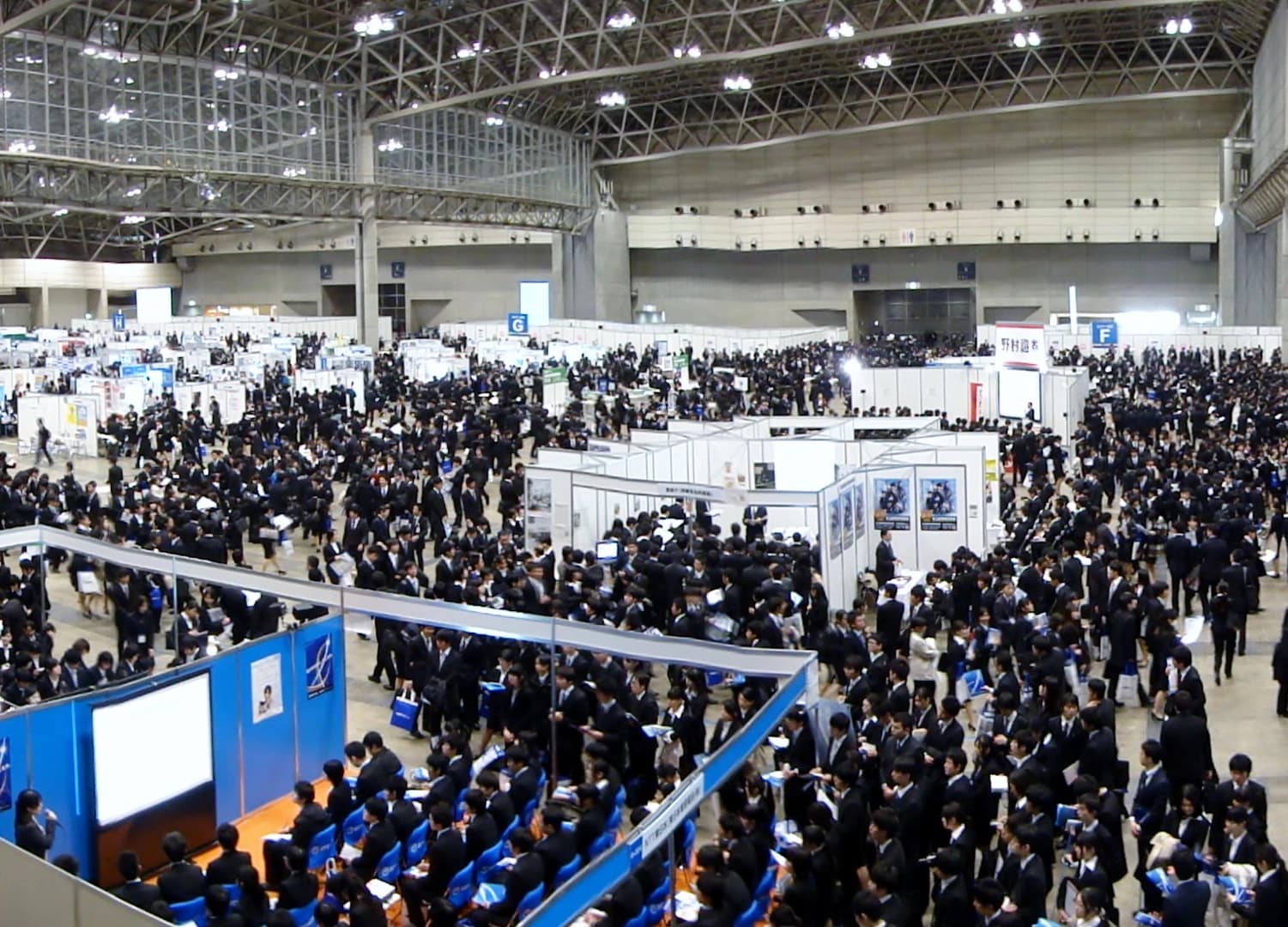 Numerous job seekers in dark suits attending a large company information session.