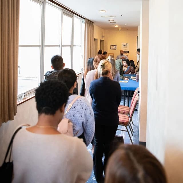 People queuing in a hallway toward a table with staff at a job fair event.