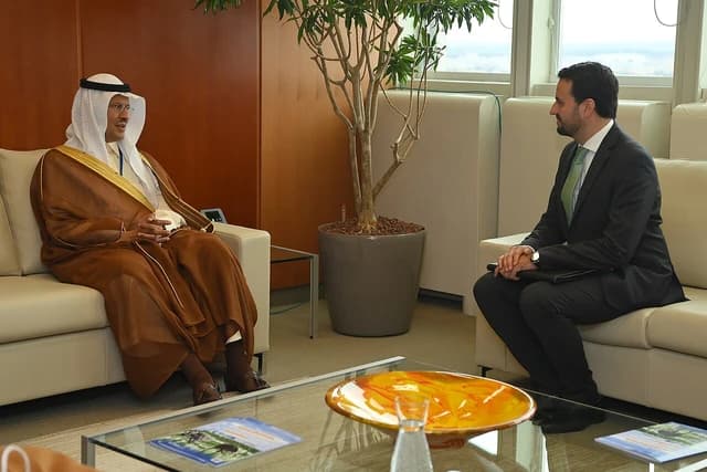 Saudi official, wearing traditional attire, sits on a sofa facing another man in a business suit.