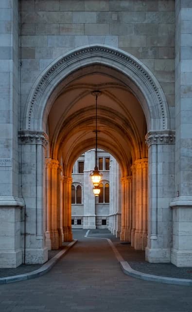 Archway of the Hungarian Parliament Building exterior featuring stone arches and illuminated lanterns.