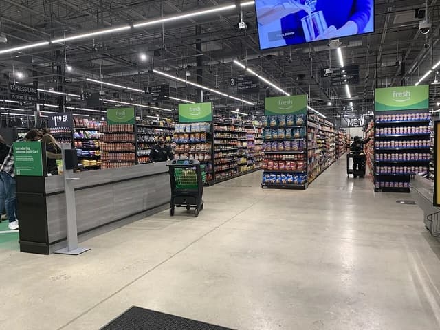 An Amazon Fresh grocery store interior with shelves stocked with food and a few shoppers.