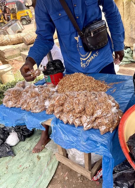 Crayfish seller bags dried crayfish for sale at an outdoor market stall in Nigeria.