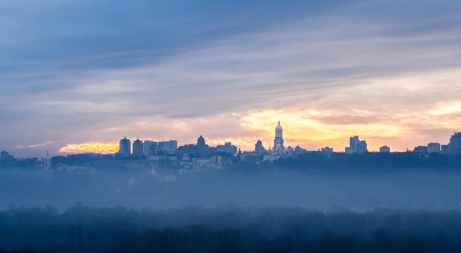 Panoramic view of the Kyiv skyline with a golden sunset or sunrise sky.
