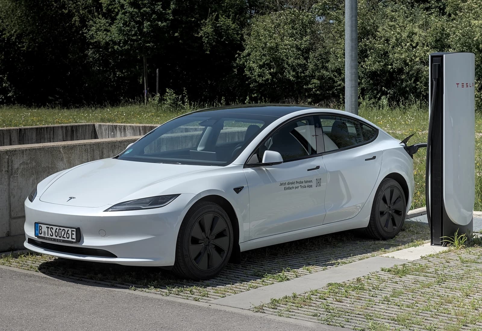White Tesla Model 3 charging at a station in a parking lot.