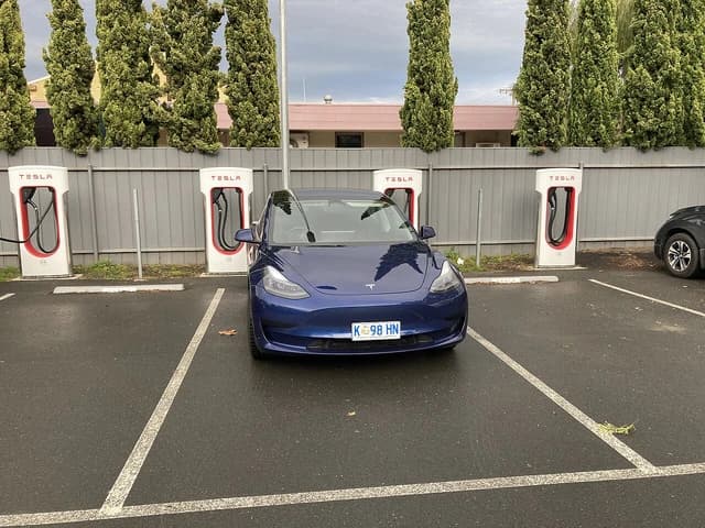 Blue Tesla Model 3 car parked at a Supercharger station.