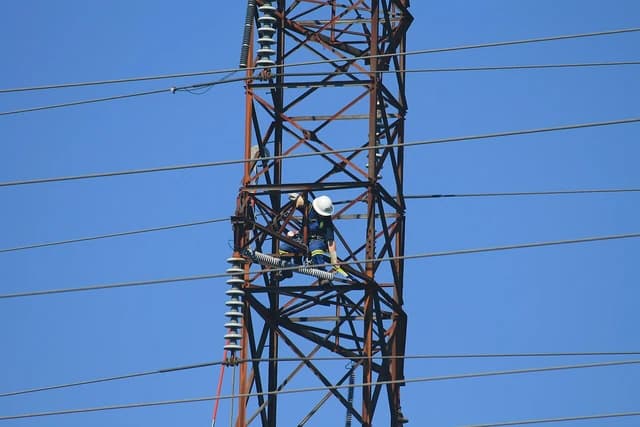Utility worker wearing a hard hat working on a metal transmission tower.