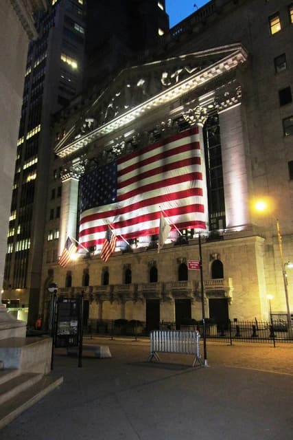 New York Stock Exchange building illuminated at night with a large American flag draped on its facade.