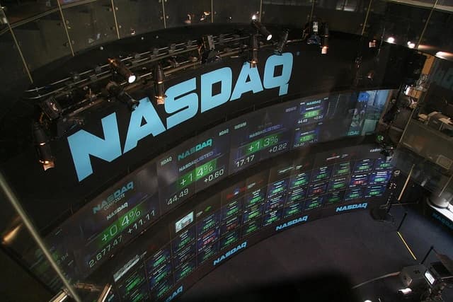 Curved digital display showing NASDAQ market data with green and red numbers.