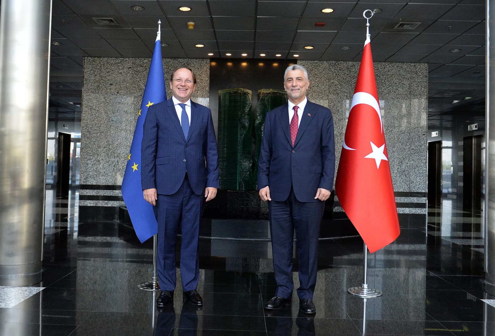 European Commissioner Olivér Várhelyi and Turkish Minister Ömer Bolat stand by flags.