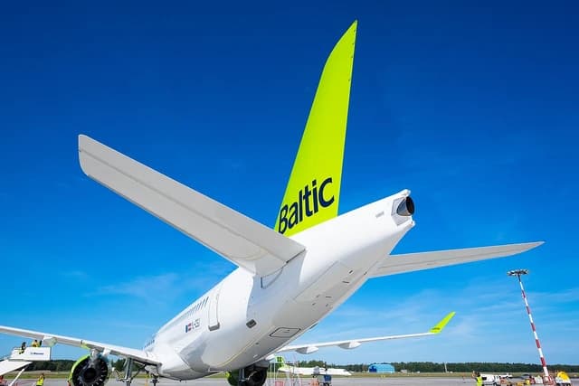 An airBaltic aircraft, seen from behind, parked at Riga Airport on a sunny day.