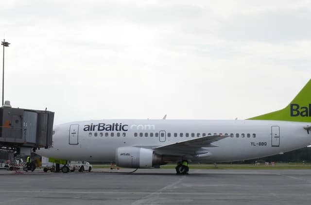 An airBaltic passenger airplane is parked at an airport gate.
