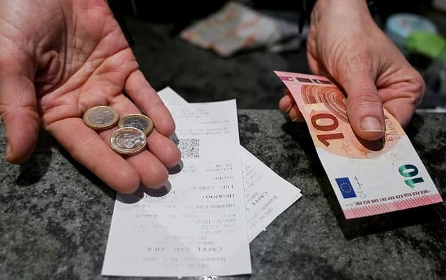 A person's hands holding Euro currency and several receipts on a dark surface.