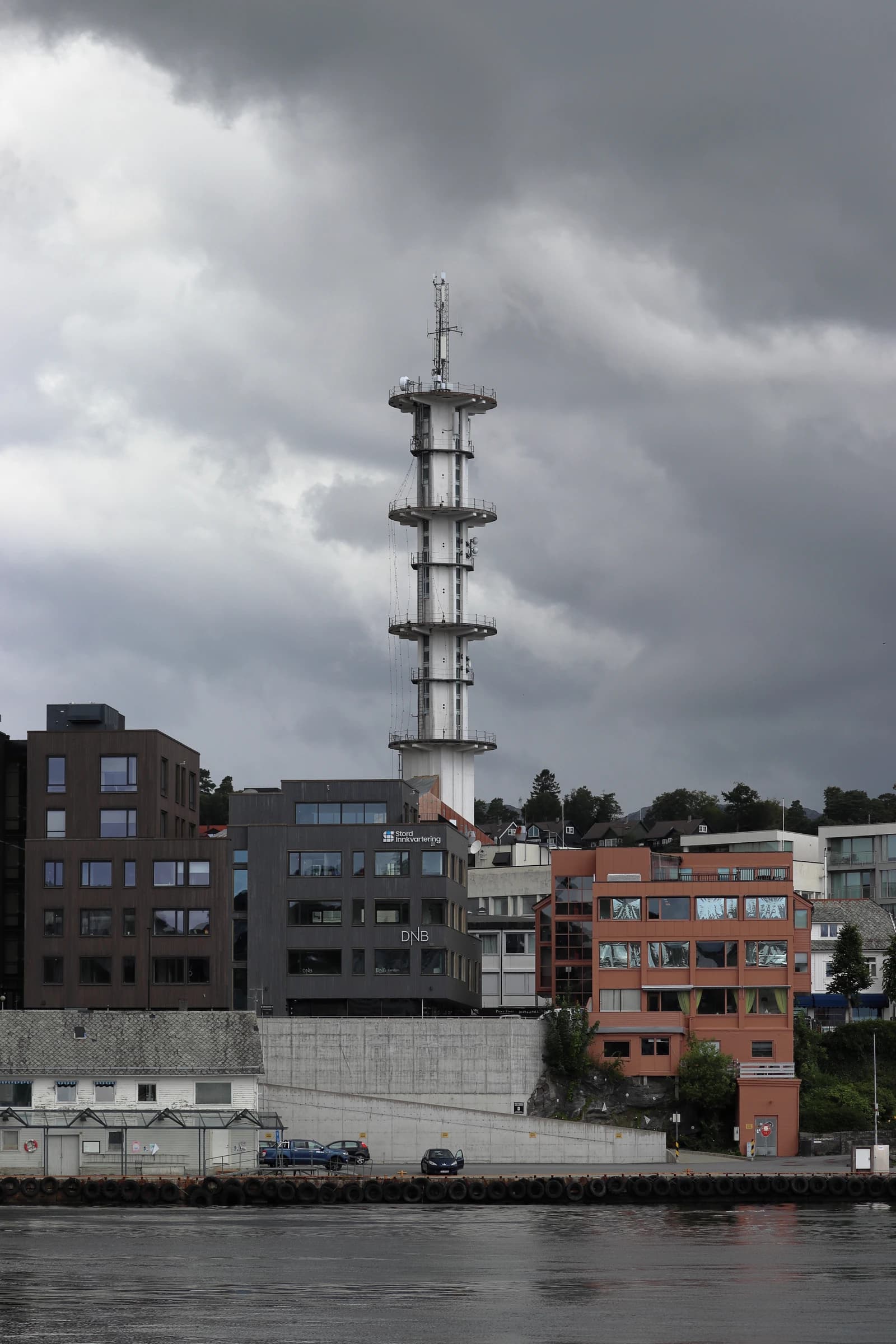 A tall white telecommunications tower rises above buildings in Leirvik, Stord, Norway.