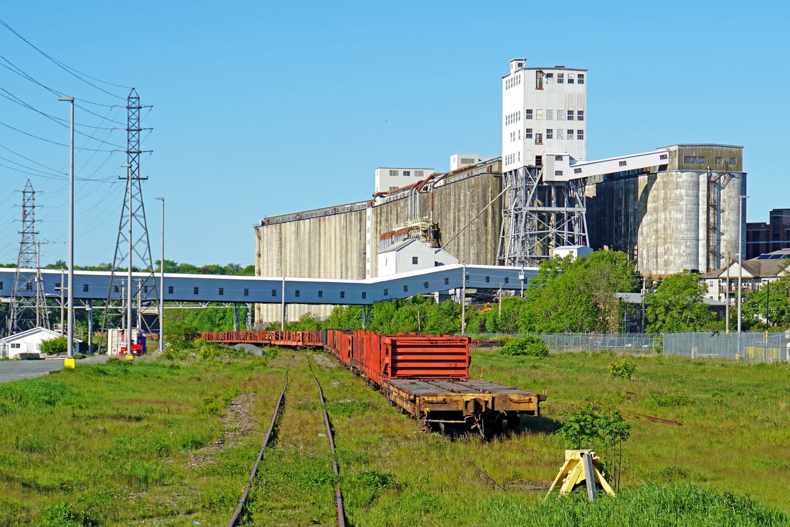 Halifax Grain Elevators stand beside railway tracks with freight cars under clear sky.