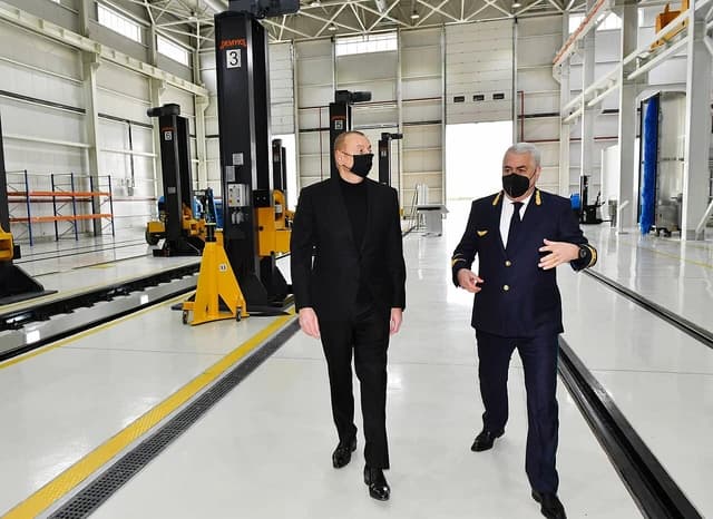 Two Azerbaijani officials, one in a suit and one in a uniform, walking inside a locomotive depot.