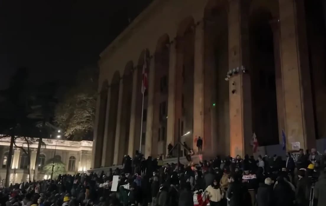 People gathered in front of a large building with columns, some carrying flags, at night.