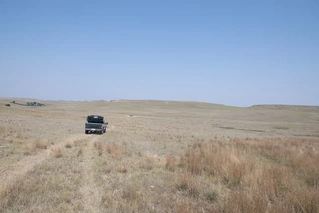 A pickup truck drives through dry, brown rangeland under a clear blue sky.