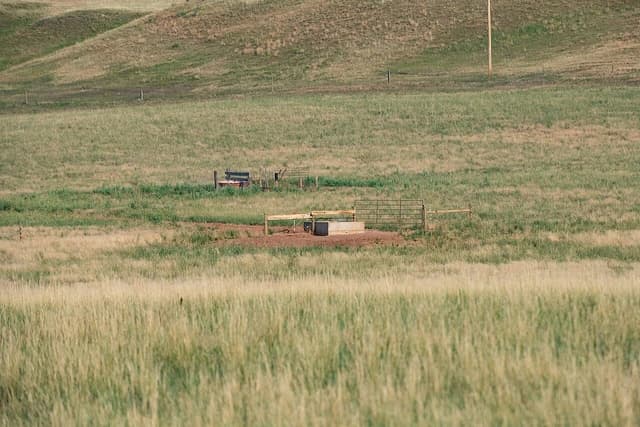 A metal water trough and a section of fencing in a large, grassy field.