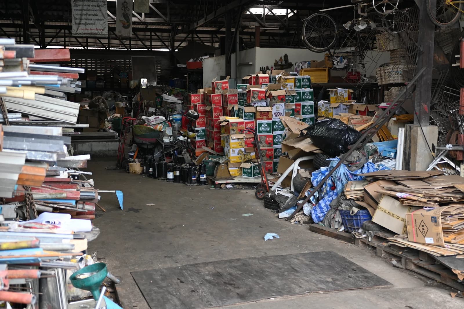 Cluttered warehouse aisle with stacked boxes, cardboard, and various tools stretching into the interior.