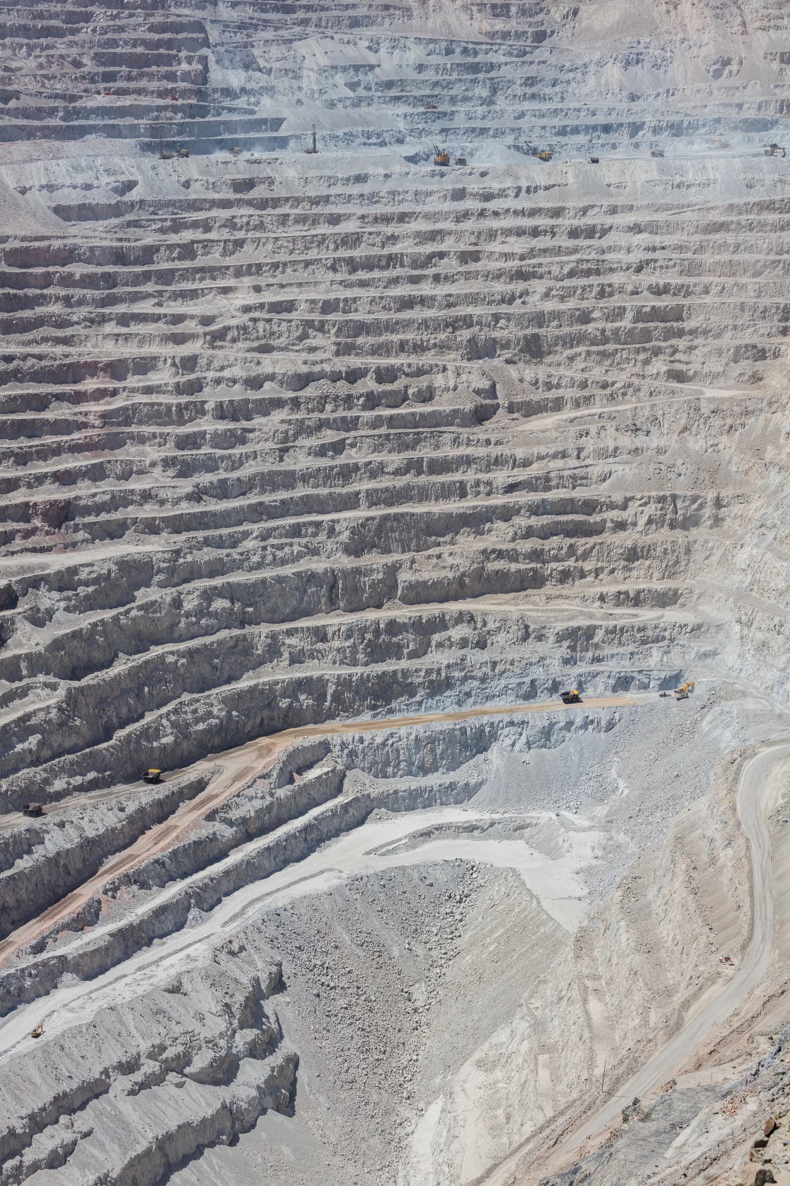 Massive open-pit copper mine showing terraced rock formations and heavy mining trucks.