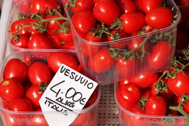 Ripe red cherry tomatoes packaged in transparent plastic punnet trays for sale.