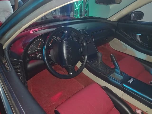 Interior of a red and black Honda NSX sports car, including the dashboard and steering wheel.