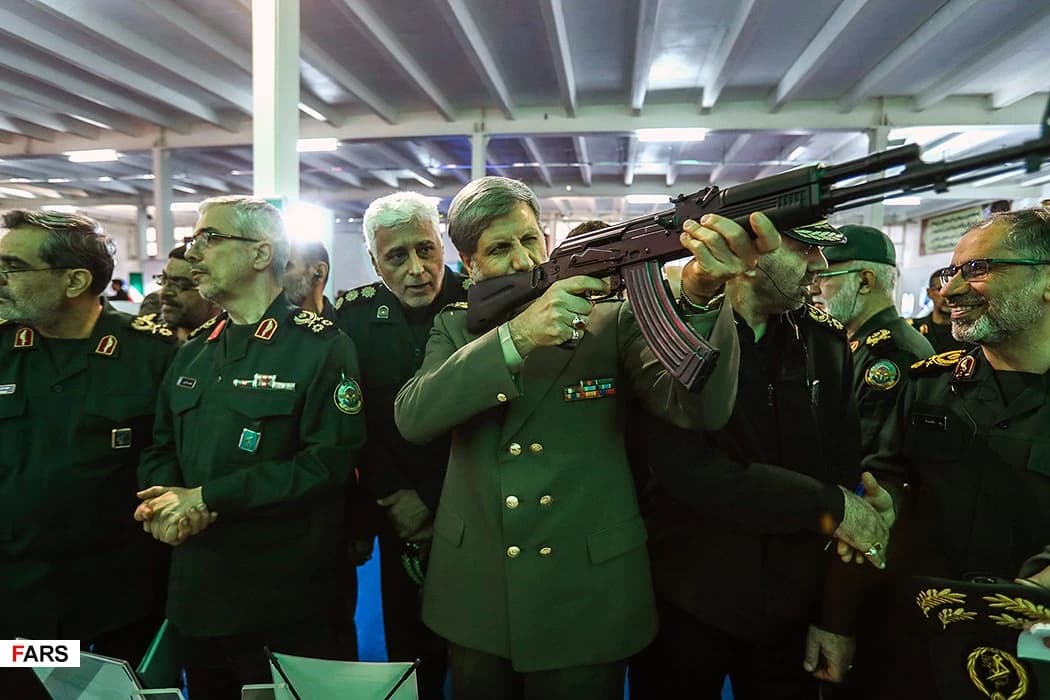 Iranian military officials, one aiming an assault rifle, at an exhibition.