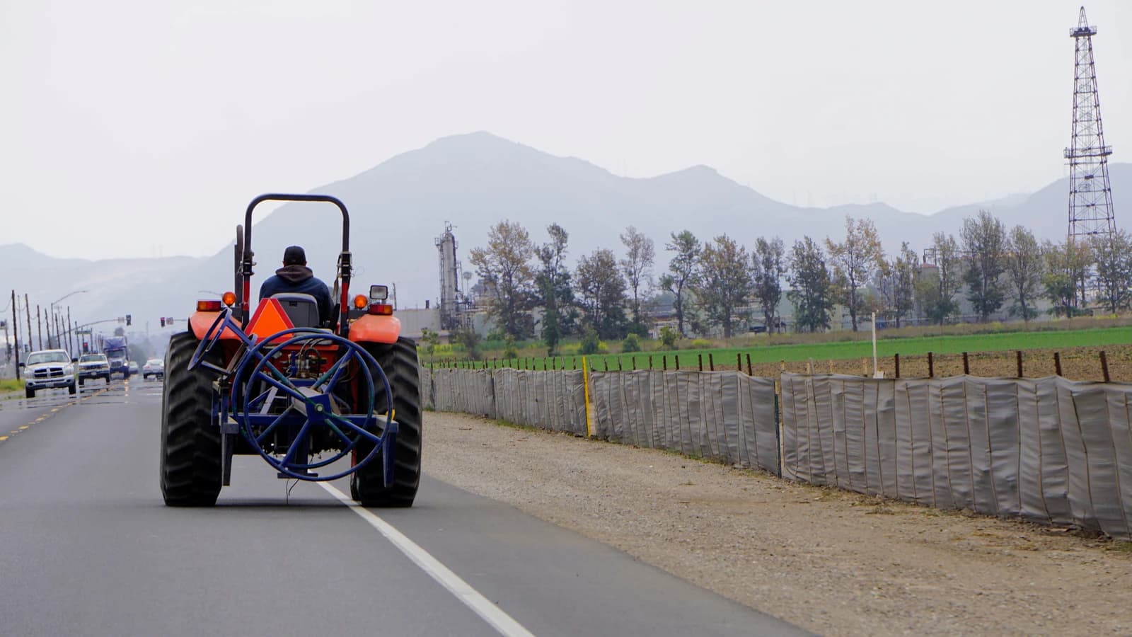 Tractor on CA34 road, Oxnard, with an oil derrick and mountains in the distance.