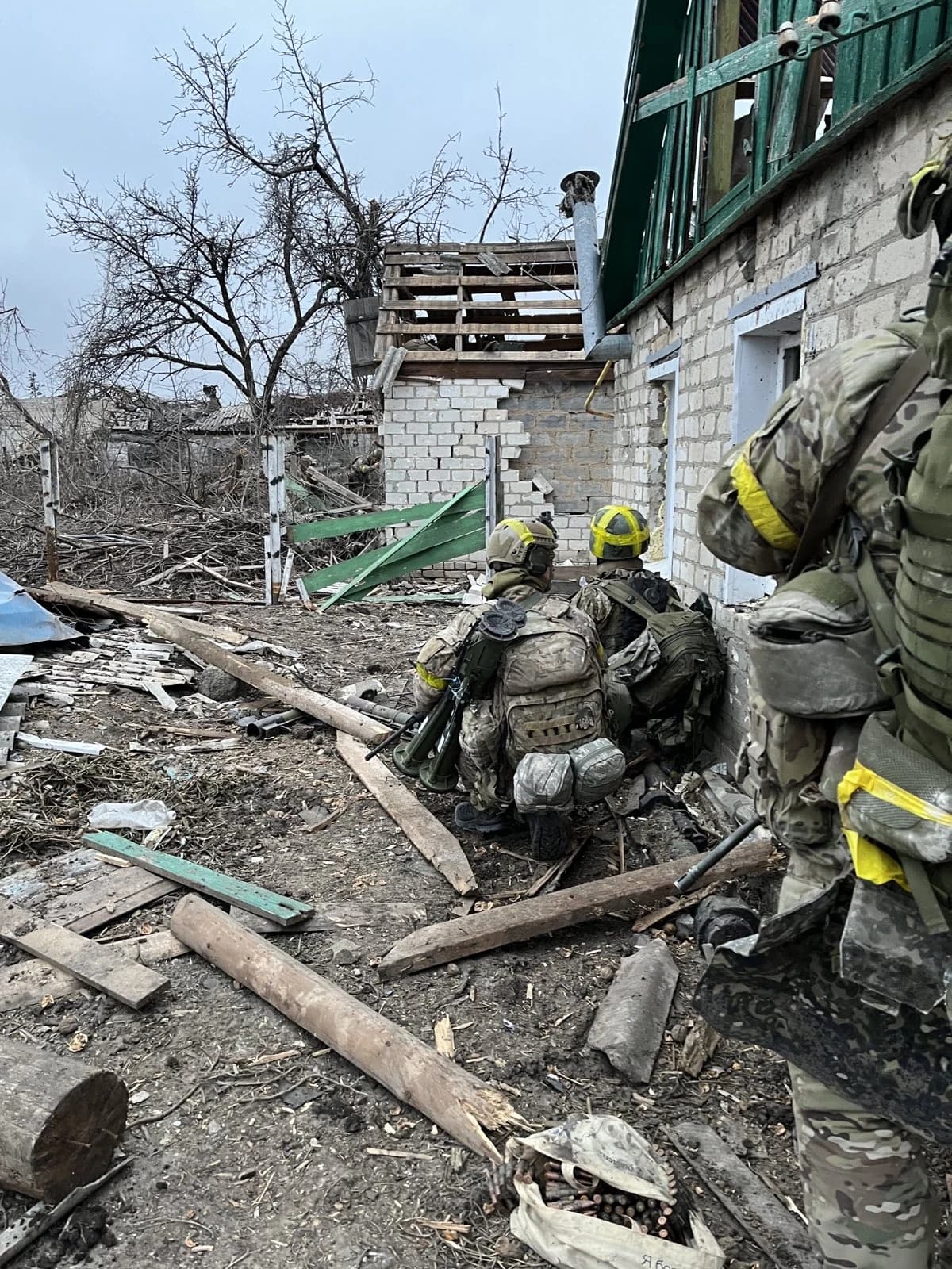 Soldiers of the 1st Battalion International Legion crouch with weapons in a combat zone.