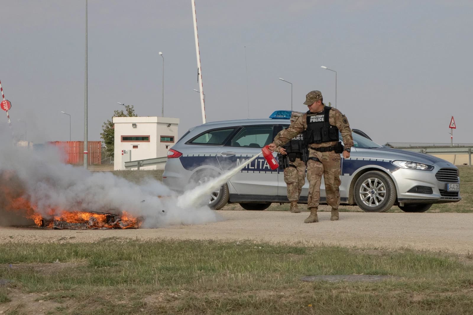 Military police officer extinguishing a small fire on the ground with a fire extinguisher.