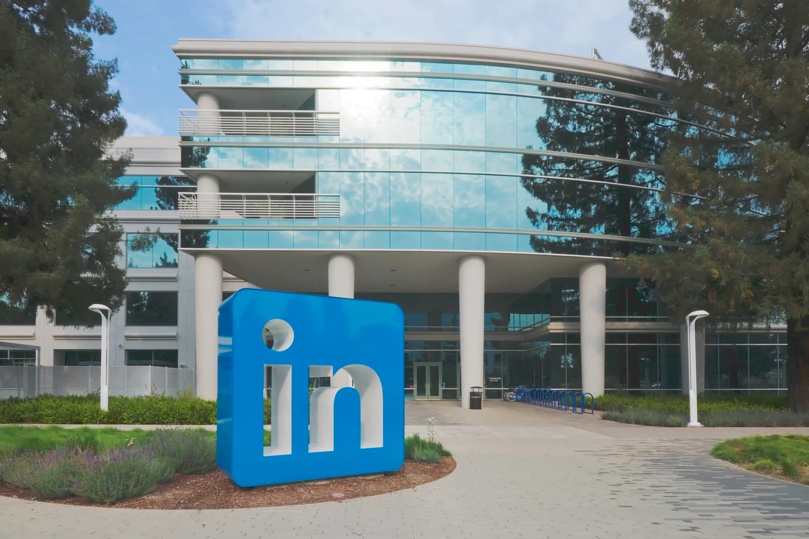 Large blue LinkedIn logo sculpture in front of a modern glass office building.