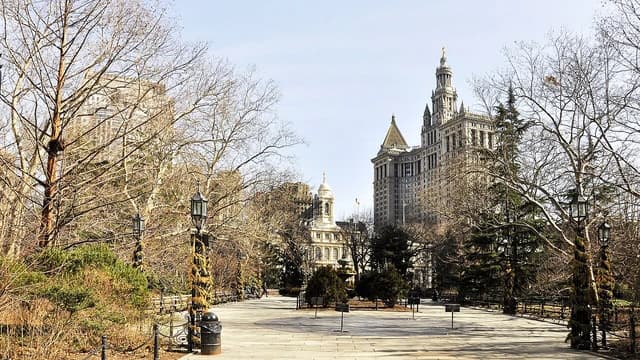 New York City Hall and Manhattan Municipal Building visible beyond park trees.