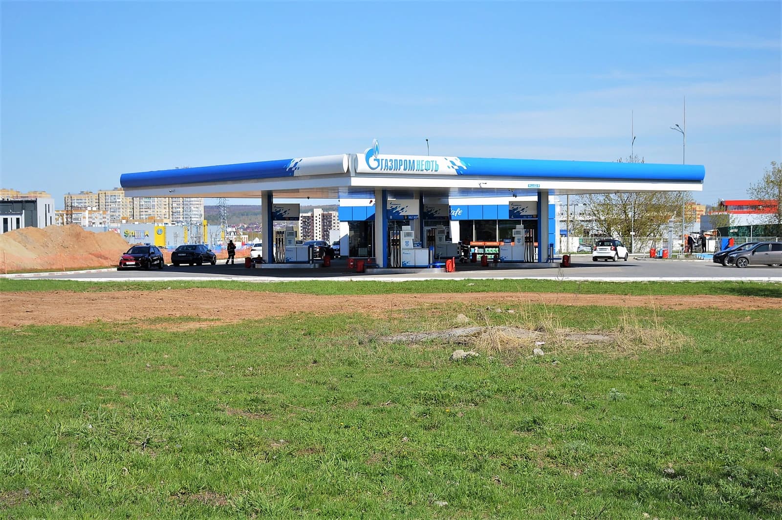 Gazpromneft gas station with several cars at pumps under a blue sky.