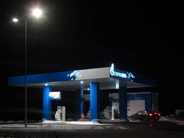 Gazpromneft gas station at night with illuminated sign, gas pumps, and a car.