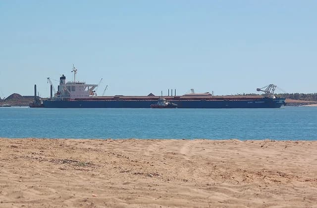 Alpha Millennium bulk carrier departing Port Hedland loaded with iron ore, with a tugboat alongside.