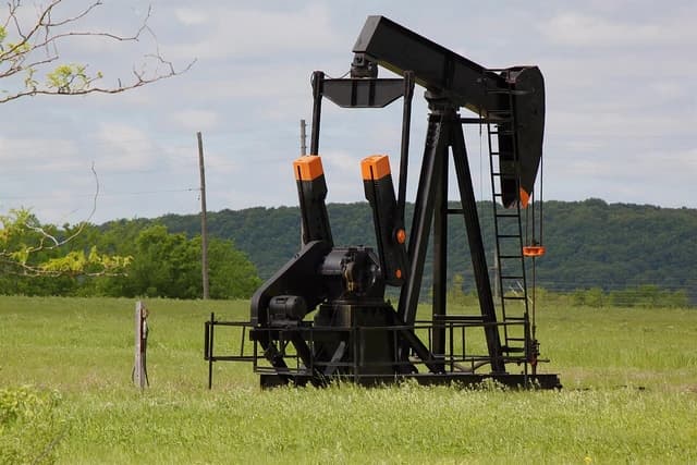 Pumpjack operates in an oil field under a partly cloudy sky.