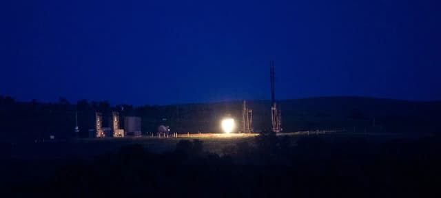 Natural gas flare burning brightly in a dark field at night.