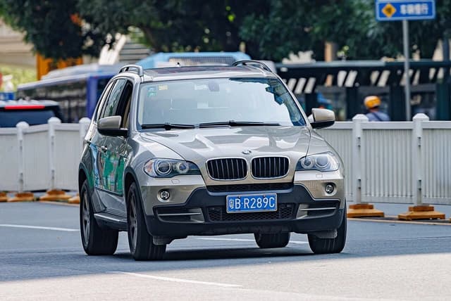A gold BMW X5 (E70) sport utility vehicle drives on a city street.