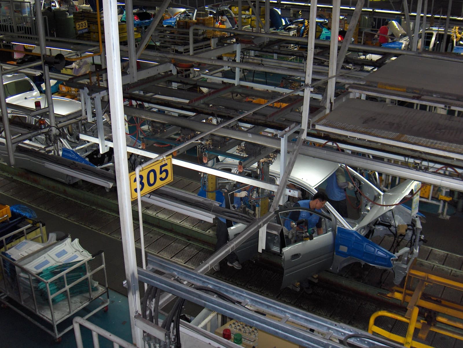 Factory workers assembling a silver car on an active production line within an industrial plant.