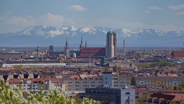 Panoramic view of Munich with city buildings and distant snow-capped mountains.