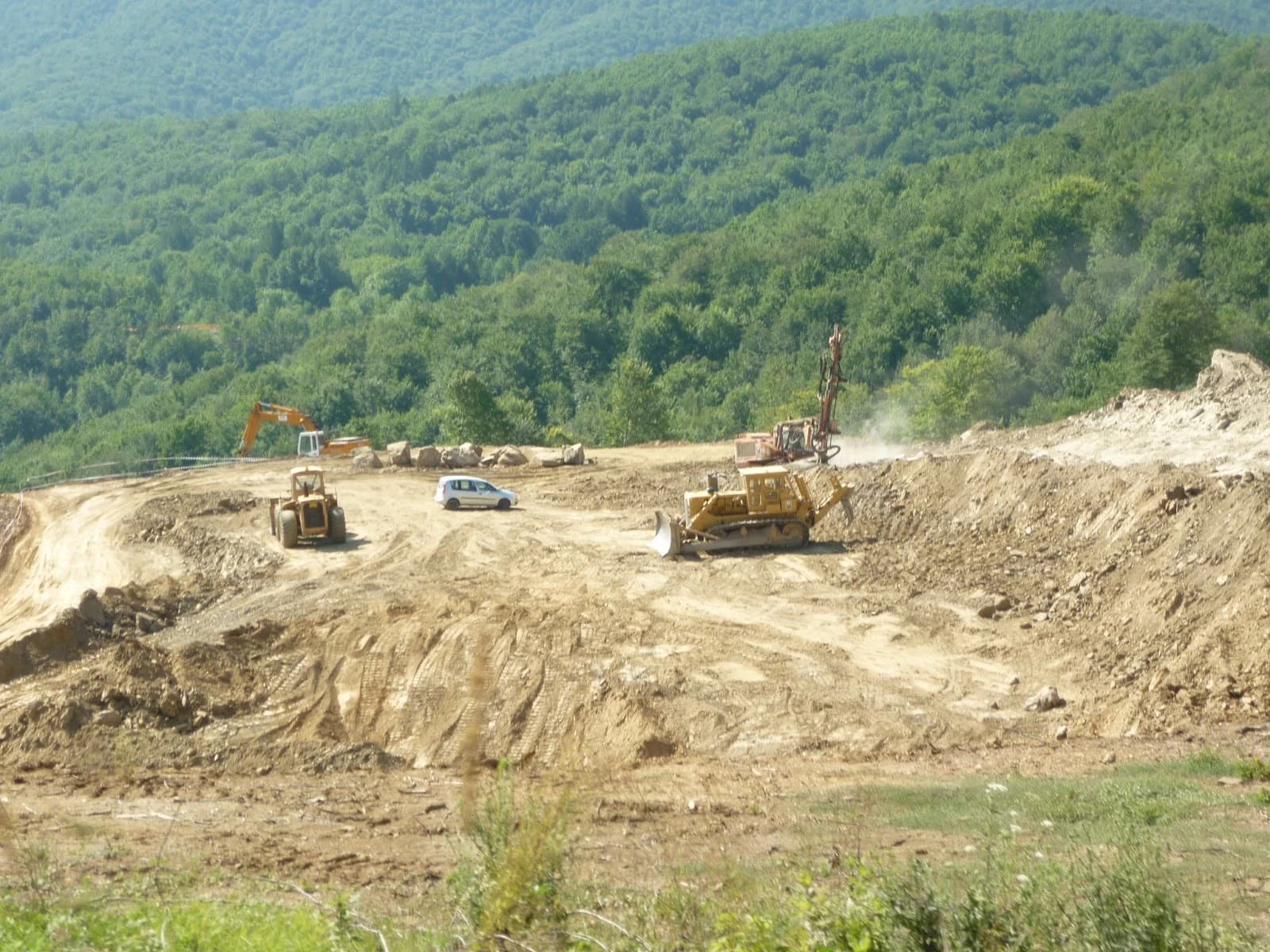 Construction machinery and a white car on a dirt track at the Skouries mining project.