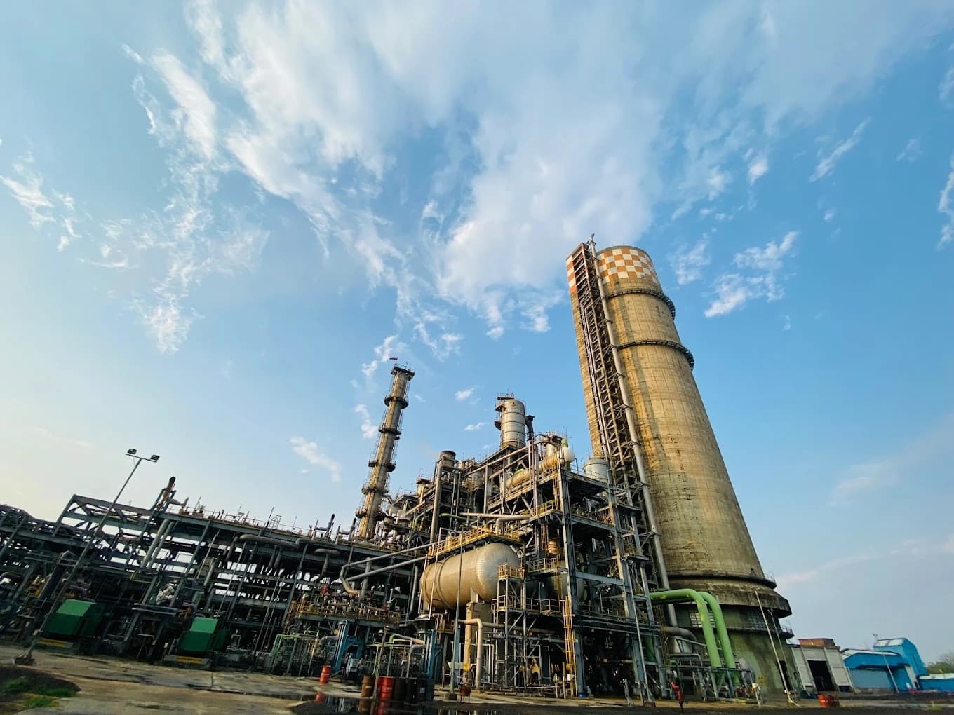 Matix Fertilizer plant with large industrial structures and a tall chimney against a cloudy blue sky.
