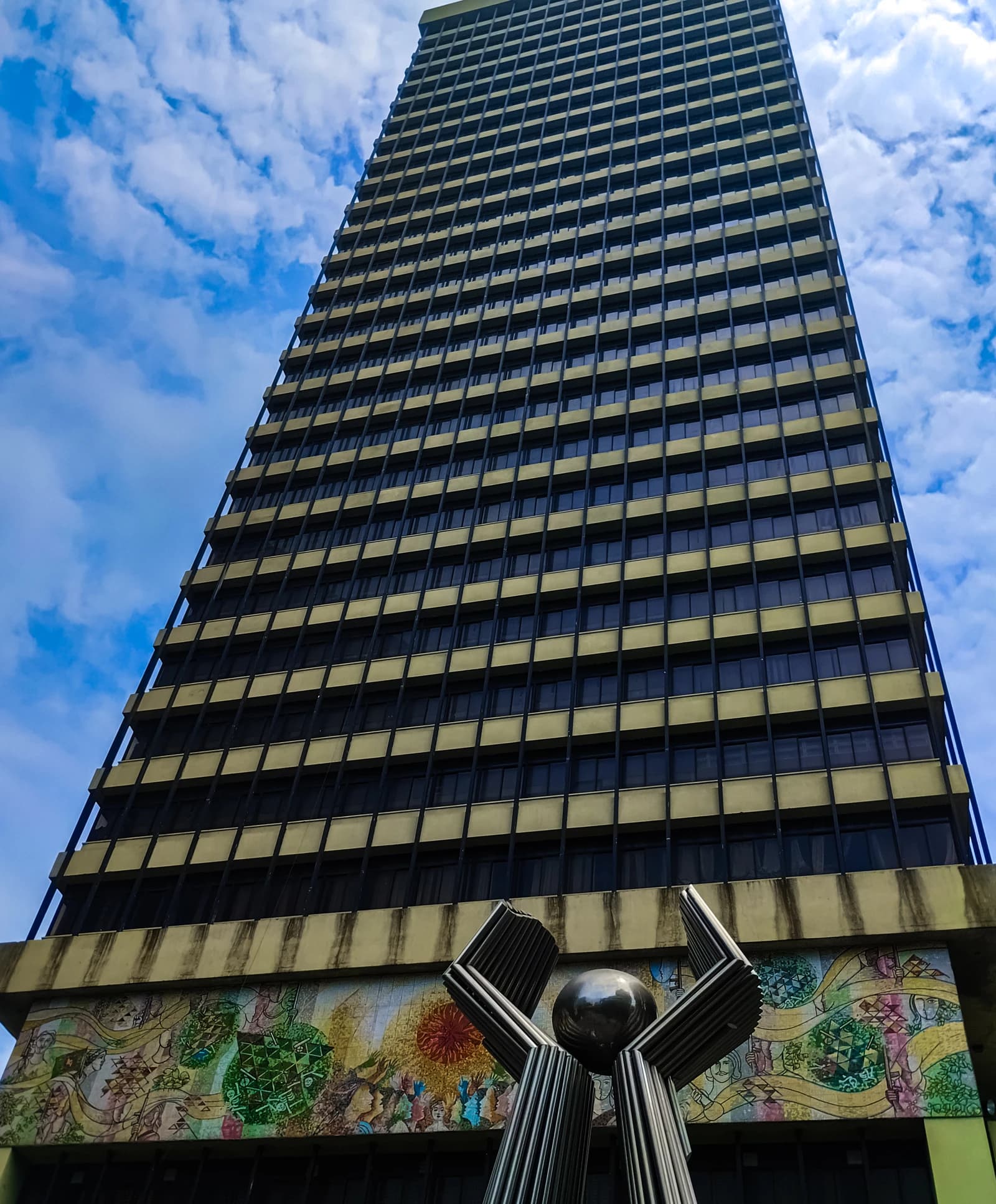 Exterior view of the Bangladesh Bank Main Building with a modern sculpture in front.