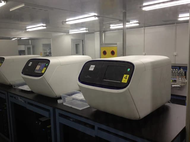 Ion Proton Sequencers, large white machines with screens, in a laboratory.